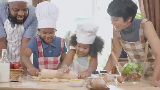 Familia afroamericana con hijo e hija rodando para la harina de trilla para cocinar con el padre y la madre juntos en la cocina en casa, los padres y los niños pequeños actividad de preparación de alimentos con diversión. - Metraje, vídeo