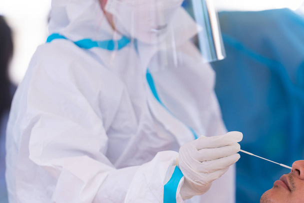 lääkäri, jolla on PPE-pukutesti koronavirus (covid-19) ihmiselle nenäpyyhkeellä antigeenitestipakkauksella. ATK. - Valokuva, kuva