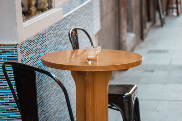 Okrągły drewniany stół ze stołkiem barowym. Szklanka z napojem kawowym - latte, cappuccino, cortado na nowoczesnym barze, kawiarnia, taras kawiarni. Hiszpański styl życia. Miejska ulica bez ludzi. Scena miejska w Madrycie. - Zdjęcie, obraz