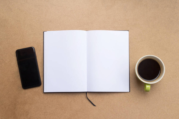 Widok z góry z pustym notebookiem, filiżanką kawy i smartfonem na brązowym tle drewnianego stołu.  - Zdjęcie, obraz
