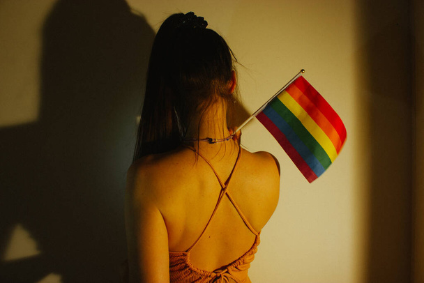 Belle femme sans visage, fille tenant le drapeau LGBT à la main pour célébrer le Mois de la fierté. Sexy fille dans l'ombre vue de dos. Drapeau arc-en-ciel est un symbole de lesbiennes, bisexuels, pansexuels, gays. Soutien LGBTQ. - Photo, image