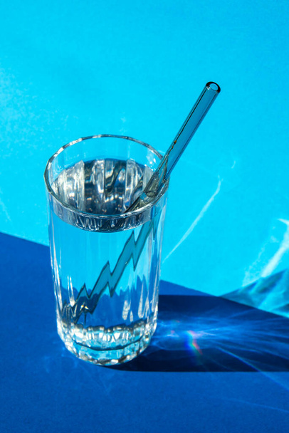 Pajitas de vidrio reutilizables en vidrio con agua sobre fondo azul Set de pajitas ecológicas para beber con cepillo de limpieza. Cero residuos, concepto libre de plástico. Estilo de vida sostenible. Residuos libres de vida Residuos bajos  - Foto, imagen