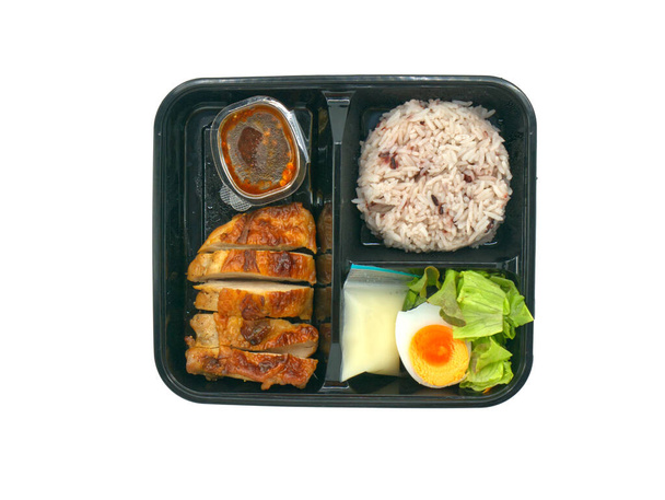 Grilled chicken breast with brown rice, spicy sauce, boiled chicken egg and salad in black colour food box, takeaway food box, isolated image on white background, top view ready to eat Thai food. - Фото, зображення