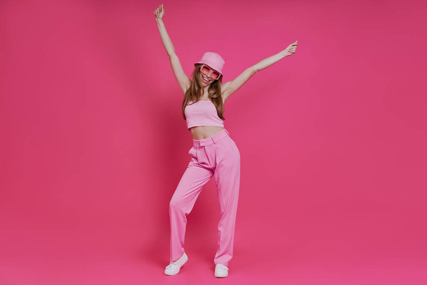 Full length of attractive young woman in trendy clothing having fun against pink background - Fotografie, Obrázek