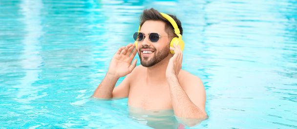 Boldog fiatalember zenét hallgat a medencében. - Fotó, kép