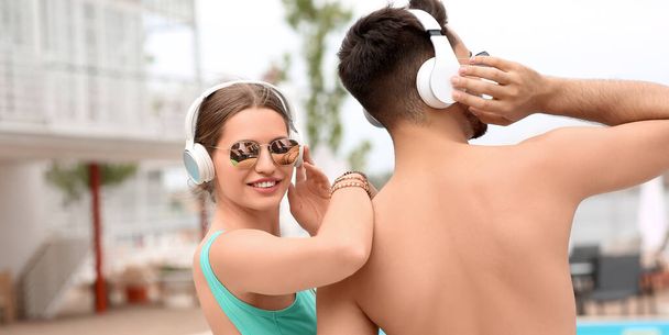 Happy young couple listening to music at resort - Photo, Image
