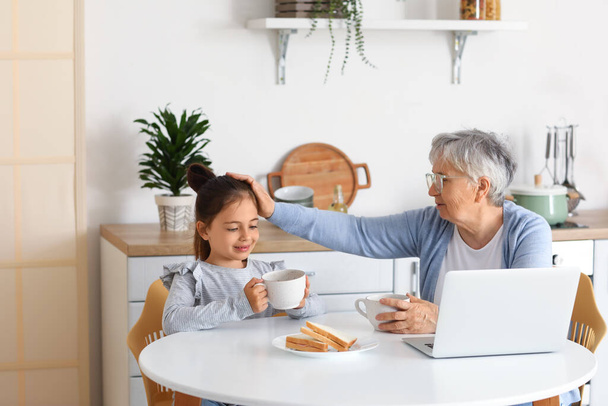 Маленькая девочка с бабушкой завтракает на кухне - Фото, изображение