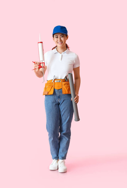 Asian female plumber with tool on pink background - Фото, изображение