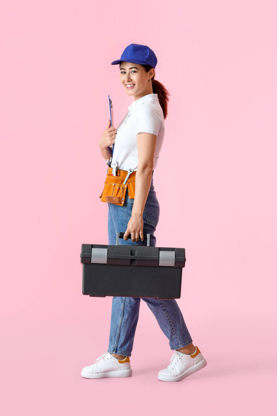 Asian female plumber with clipboard and bag on pink background - Zdjęcie, obraz