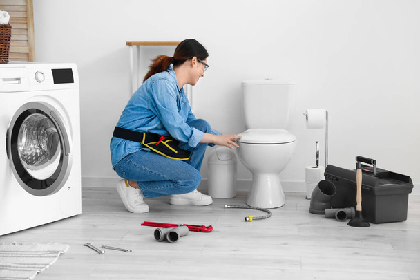 Asian female plumber fixing toilet bowl in bathroom - Photo, Image