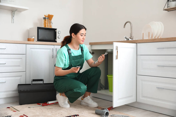 Asian female plumber with wrenches near sink in kitchen - Foto, immagini