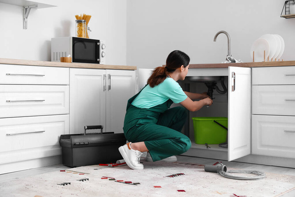 Female plumber fixing sink in kitchen - 写真・画像