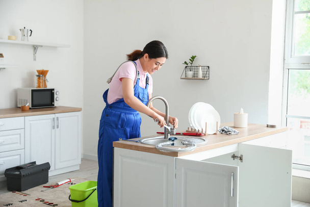 Asian female plumber fixing sink with plunger in kitchen - Photo, Image