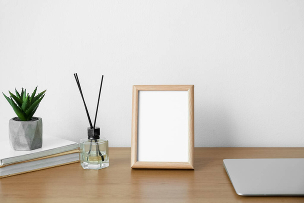 Blank frame and reed diffuser on table near light wall - Photo, Image