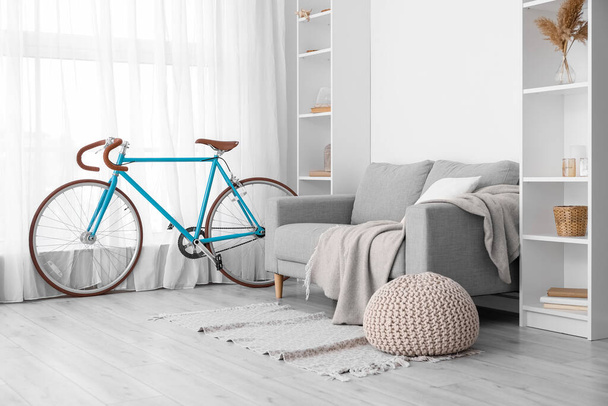 Інтер'єр світлої вітальні з велосипедом, сірим диваном і стелажами
 - Фото, зображення