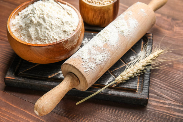 Oreja de trigo, tazones con harina, rodillo y tabla sobre fondo de madera, primer plano - Foto, imagen