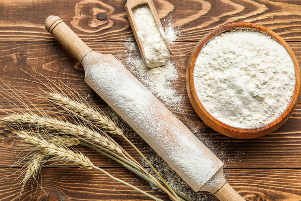 Orejas de trigo, rodillo, cuchara y tazón con harina sobre fondo de madera - Foto, imagen
