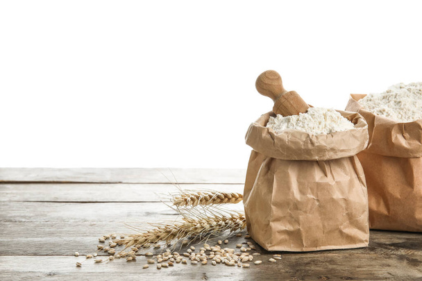 Bolsas de papel con harina, cucharada y espigas de trigo sobre mesa de madera sobre fondo blanco - Foto, Imagen