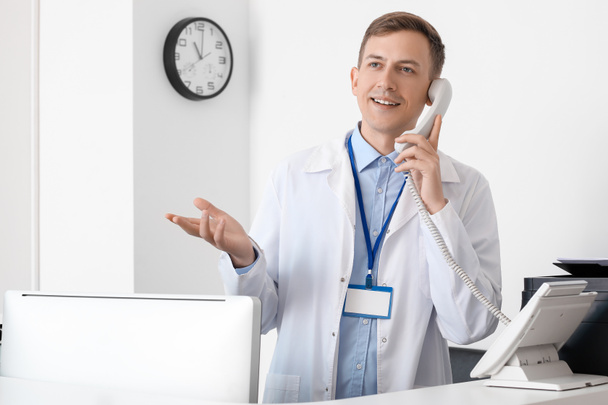 Чоловічий прийом розмовляє по телефону за столом у клініці
 - Фото, зображення