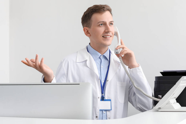 receptionist maschile parlare per telefono alla scrivania in clinica - Foto, immagini