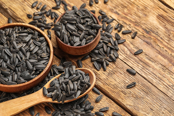 Tigelas e colher com sementes de girassol preto no fundo de madeira, close-up - Foto, Imagem