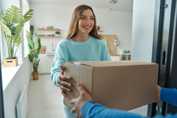 Happy young woman accepting box from delivery man at home - Foto, Bild