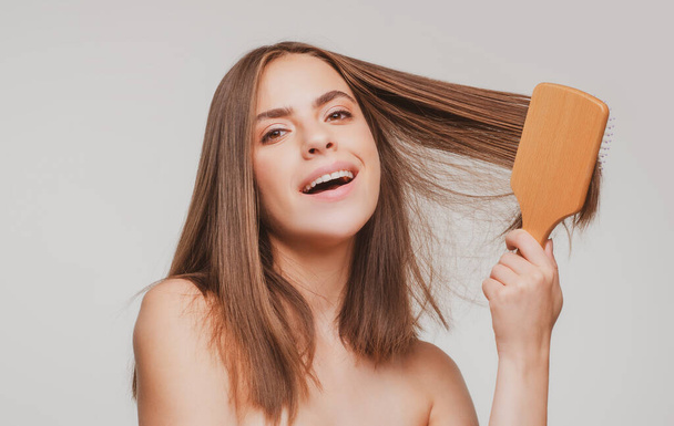 Smiling woman combing healthy and shiny hair, isolated on studio - Valokuva, kuva