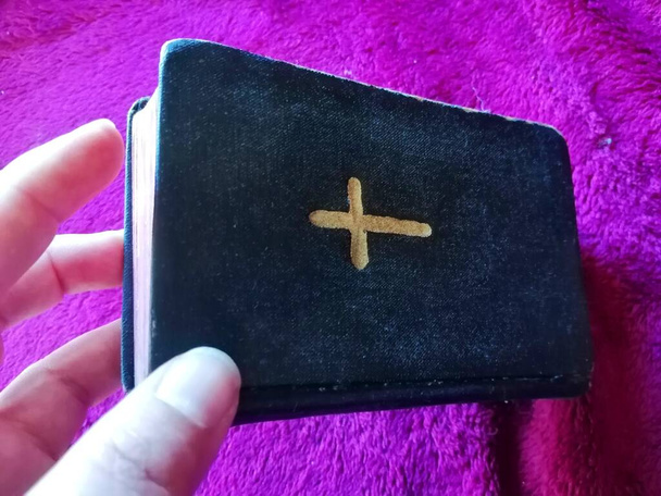 Маленькая книжка с крестом. Рука держит исторический мини молитвенник.  - Фото, изображение
