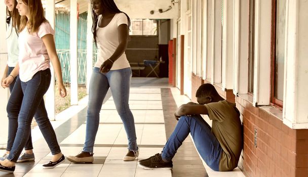 Młody chłopiec siedzi sam w szkole ze smutnym uczuciem. Afrykańskie dziecko w depresji porzucone w korytarzu i opierające się o ceglany mur. Koncepcja znęcania się, dyskryminacji i rasizmu. - Zdjęcie, obraz