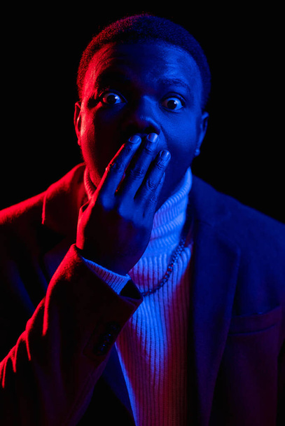 Shocked man. Omg face. Wow portrait. Unexpected surprise. Astonished speechless guy in neon light covering mouth in unbelievable emotion on dark background. - Foto, Imagem