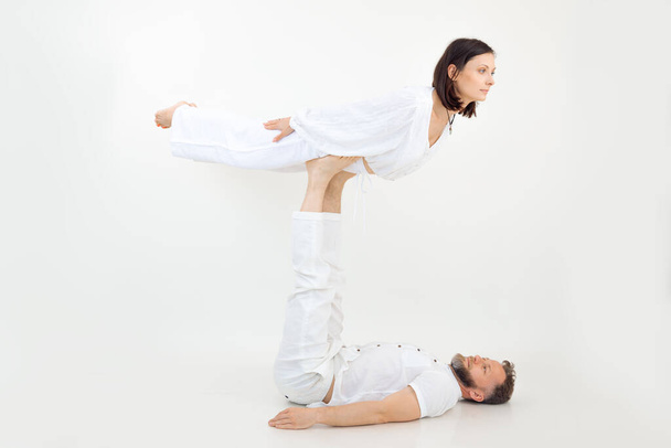 Man and woman, family doing sports exercises, fitness and yoga. Healthy lifestyle. Male holding female on legs, practicing postures, spirituality and zen acrobatics. Trust in pair couple. White view - Foto, immagini