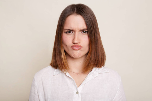 Image of Caucasian dark haired attractive woman wearing shirt, looking at camera with pout lips, being sad and confused, posing isolated over white background. - Valokuva, kuva