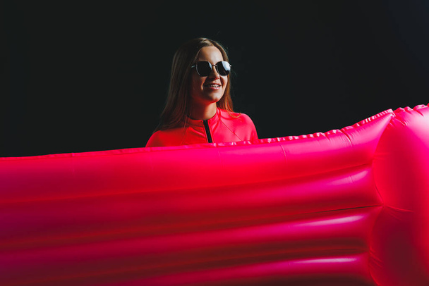 Beautiful woman dressed in pink swimsuit and sunglasses posing with pink inflatable mattress isolated on green background - Photo, Image