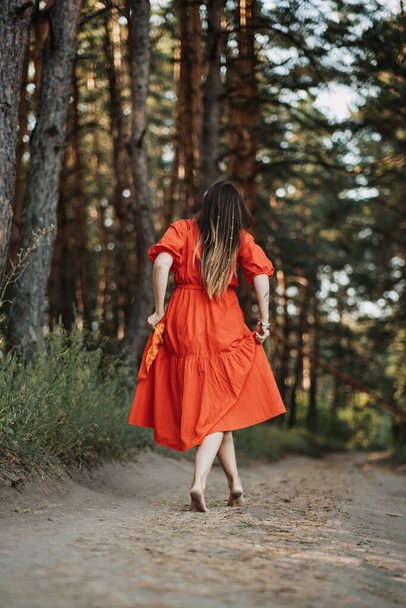 Barefoot happy young woman in red dress with hand raised dancing in pine forest at summer day. Mindfulness, wellbeing, Mental health, wellness, world mental health day, think positive concept. - Photo, Image