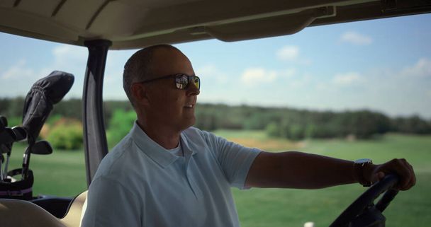 Golf arabasına doğru yürüyen lüks bir golfçü. Zengin adam golf kulübünde arabasıyla oturuyor. Gülümseyen işadamı arabaya biniyor. Yaşlılar güneşli bir sabahta aktif emekliliğin tadını çıkarıyorlar. Boş zaman konsepti. - Fotoğraf, Görsel