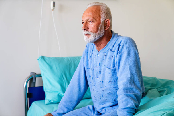 Thoughtful elderly male patient in hospital bed in ward room. Healthcare people problem concept - Photo, image
