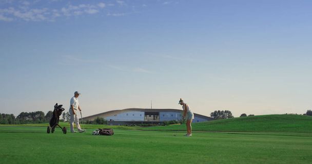 Professional golf people play game on fairway. Couple practice on sunset course. Coach team enjoy spending time at country club. Two golfing players training on summer field. Sport leisure concept. - Fotografie, Obrázek