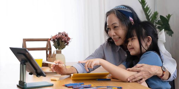 Rakastava vanhempi isoäiti halata olkapäät pieni tyttö lapsenlapsi auttaa valmistelussa kotitehtäviä tukea antaa neuvoja. Ystävällinen ikäinen nainen opettaja katsomassa pieni lapsi oppilas kirjallisesti matematiikka ongelma solutio - Valokuva, kuva