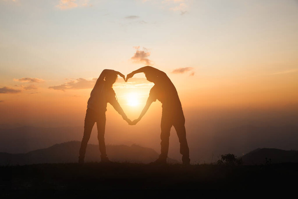 A woman and a man make a heart at sunrise on the mountain. god is love concept heart shape mountain travel manifestation of love love and feelings - Photo, Image