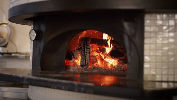 キッチン石オーブン薪を焼くarイタリアのピザレストラン。スローモーションで炉暖炉のベーカリーストーブで点火本物の火の炎を閉じます。伝統的な本格的な料理おいしい料理のコンセプト. - 写真・画像