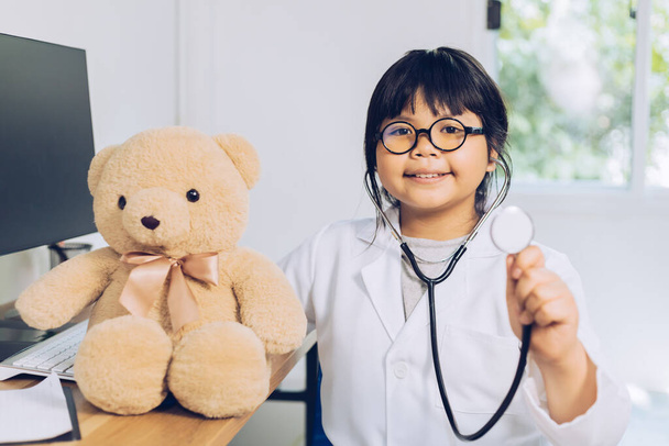 Uma criança vestida de médico se senta e examina um ursinho de pelúcia no hospital. - Foto, Imagem