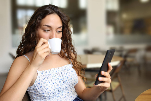 Kahve içen ve barda oturan akıllı telefonları kontrol eden bir kadın. - Fotoğraf, Görsel
