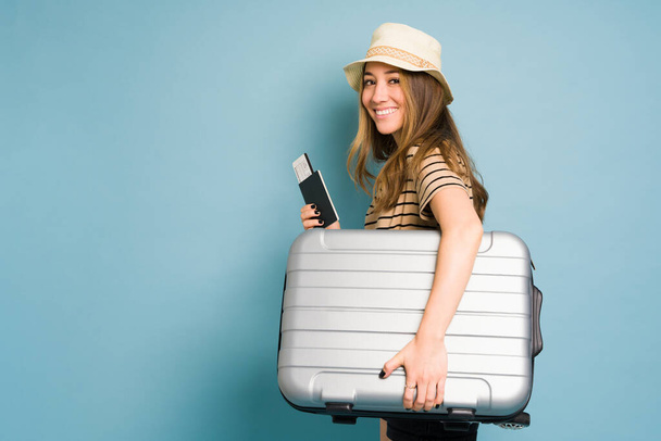 Όμορφη λευκή γυναίκα κουβαλάει μια βαλίτσα και φαίνεται έτοιμη για ένα ταξίδι σε ένα στούντιο. - Φωτογραφία, εικόνα