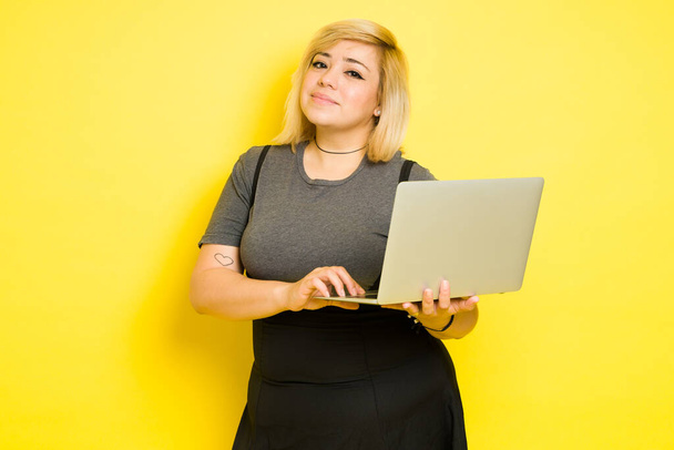 Portré egy kocka pufók nő kezében egy laptop, miközben áll szemben a sárga háttér - Fotó, kép