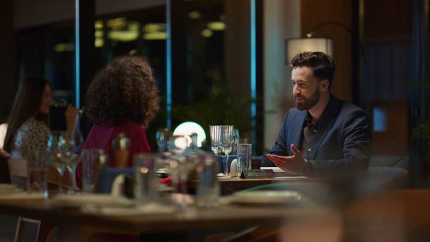 Multiracial lovers chatting talking together in night hotel restaurant. Joyful couple sitting on romantic dinner date. Two people celebrating anniversary in fancy cafe. Enjoying time together concept. - Photo, Image