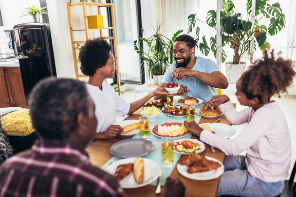 夕食のテーブルで食べ物を楽しむ多世代のアフリカ系アメリカ人の家族. - 写真・画像