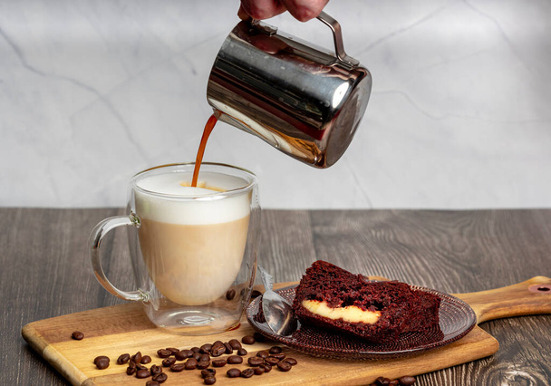 Zwarte koffie wordt gegoten in een glazen mok met schuimmelk. Bereiding van koffie latte. - Foto, afbeelding