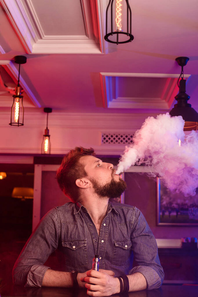 Βέιπ. Αστραφτερός άνθρωπος σε ένα σύννεφο ατμού. Η φωτογραφία τραβήχτηκε σε ένα μπαρ. Μαγαζί με κασέτες - Φωτογραφία, εικόνα