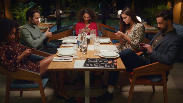 Tabela de amigos lendo telefone celular navegando internet mídias sociais no restaurante. Multiracial grupo reunião partilha mesa de café à noite. Jovens ignorando uns aos outros no bar. Conceito de tecnologia. - Foto, Imagem