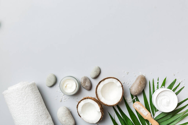 Coconut with jars of coconut oil and cosmetic cream on colored background. Top view. Free space for your text. Natural spa coconut cosmetics and organic treatment concept Coconut Spa composition. - Foto, Imagen